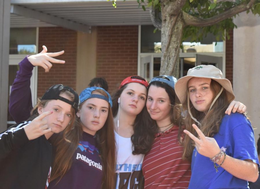 Group of freshman pose with upperclassmen in courtyard dressing up as boys with backwards hats, and polos.