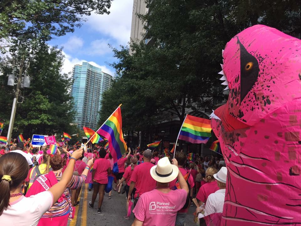 Planned Parenthood activists walk in the 2017 Atlanta Pride Parade alongside a marcher dressed in a dinosaur costume. The annual parade is a festive event with attendees often wearing bright colors, dressing in costumes and showing their pride with rainbow accessories.
