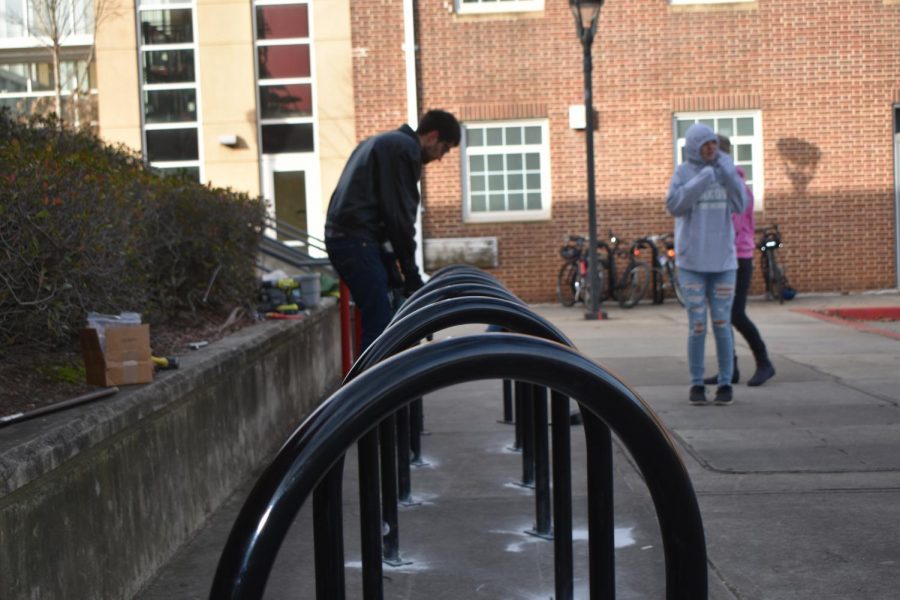 Scott Ehardt, a member of SOPO Bikes Cooperative, helps students install the bike racks as he drills a hole into the ground for the pump.