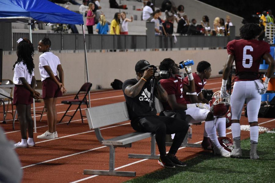 Former Grady quarterback Simeon Kelley (left) focuses the camera on the action from the bench as senior tight end Dewan Wright (center) squeezes a swig of water and current quarterback and senior Aquinas Stillwell (right) takes a breather. Kelley, now a photographer for Atlanta Public Schools, led the Knights to an undefeated regular season and state semifinals finish in 2005.
