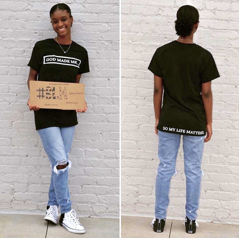 Swint poses with a Black Lives Matter sign to show her support. She shows the front and back design of one of her t-shirts.