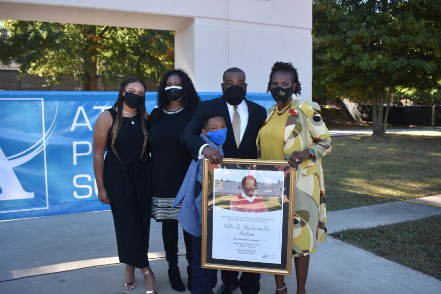 Henderson family members pose with a framed tribute banner, with details about the ceremony inscribed. His son, daughter, and grandchildren were all present for the occasion. 