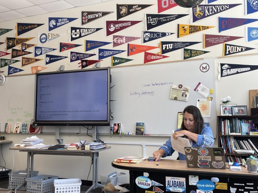 AP English Literature and Composition teacher Susan Barber grades practice essays for the AP exam while displaying final exam dates on her board. Many students are required to take both a  final and an AP exam for a course at the end of the year.