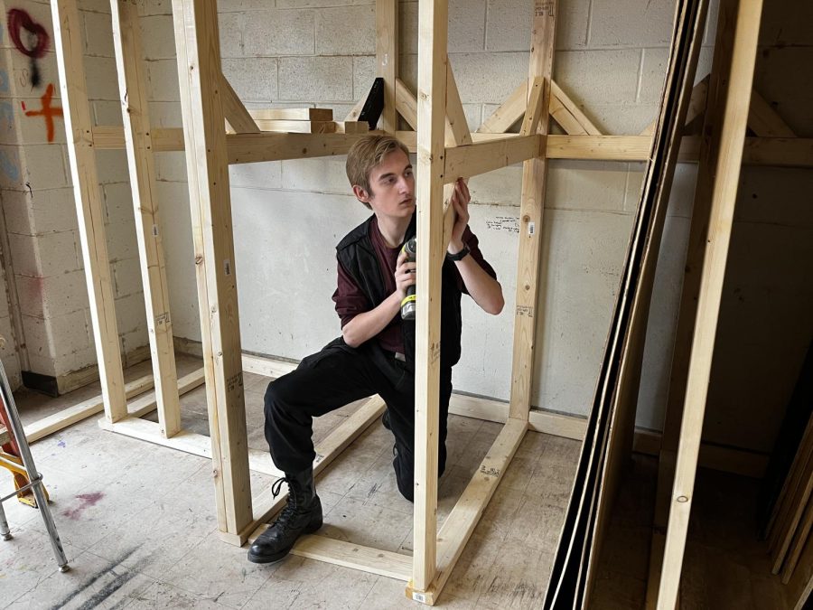 Senior Nolan Simpson screws wood planks together with a drill to build a plywood rack.
