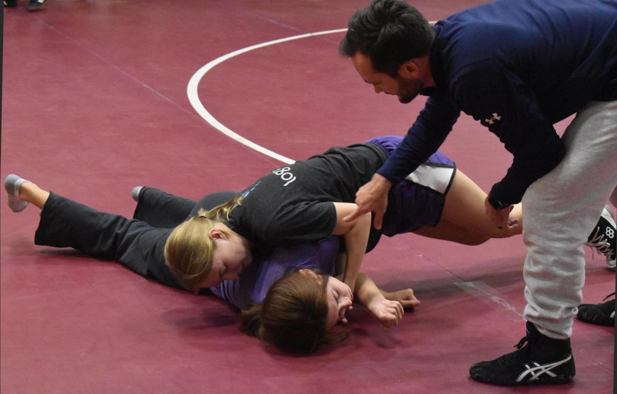 Juniors Emma Jordan and Taryn Thomson receive instruction from Assistant Coach Brooks Smith at a practice on Dec. 2. After being introduced to wrestling only a month prior, they need to learn the techniques and hand placements that are crucial to success in wrestling.