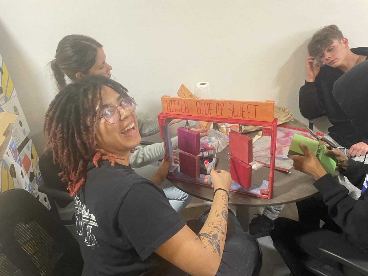 Co-facilitator of the Chocolate Club and Kennesaw State University sophomore ZiaKenya Saiz (left) assists Midtown senior Scottie Devey (right) with creating a display about sustainable chocolate harvesting based on the novel "The Bitter Side of Sweet” by Tara Sullivan.