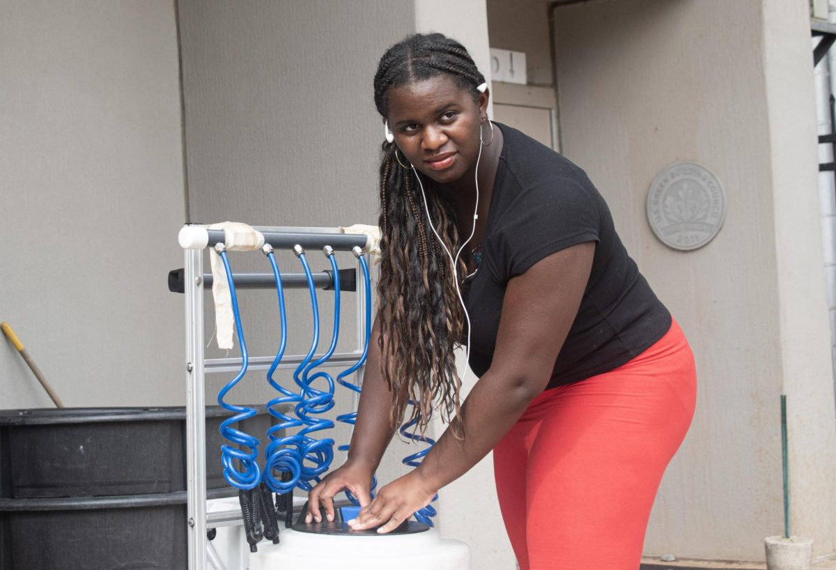 Student Athletic Trainer Aria Shaw prepares the "cow" hydration system before football practice, ensuring the players have access to cool water during the intense Atlanta summer.