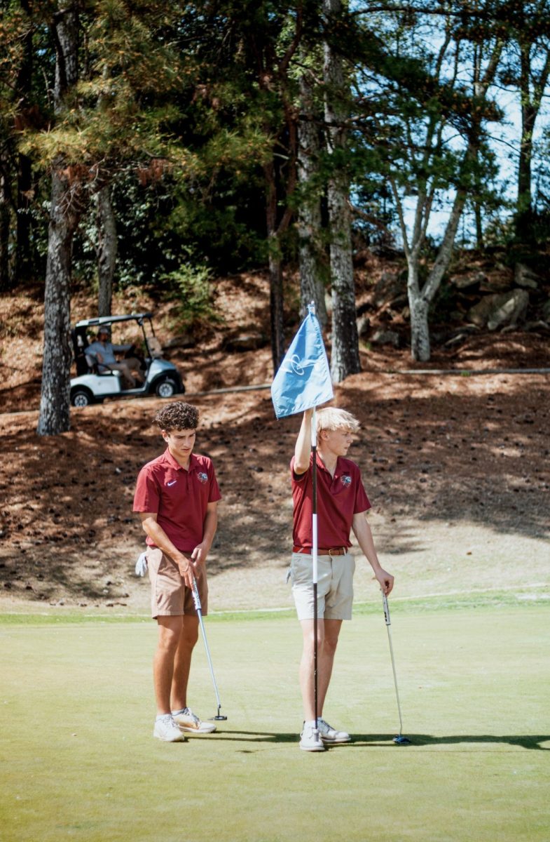 Senior co-captain Carter Klein sinks a putt as Senior co-captain Davis Fenger holds the flag for him. The pair shot six under and finished tenth at the Brookwood Boys invitational.
